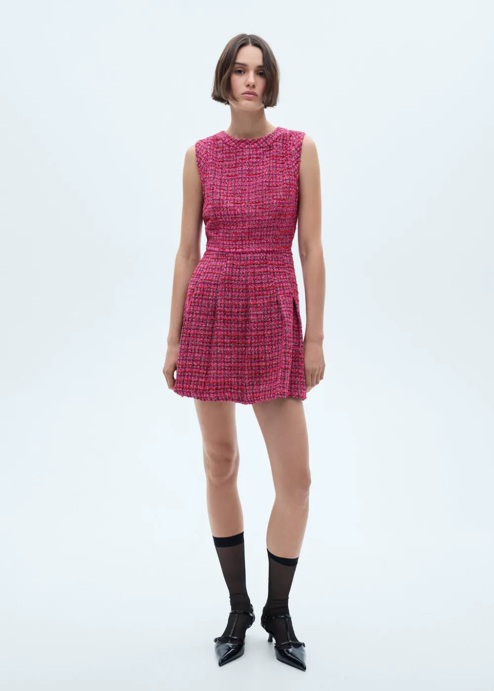 Chic woman in a textured pink dress, paired with sheer black socks and stylish shoes, showcasing elegant wedding guest outfit